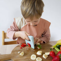 Child cutting fruits on a wooden board with a white background